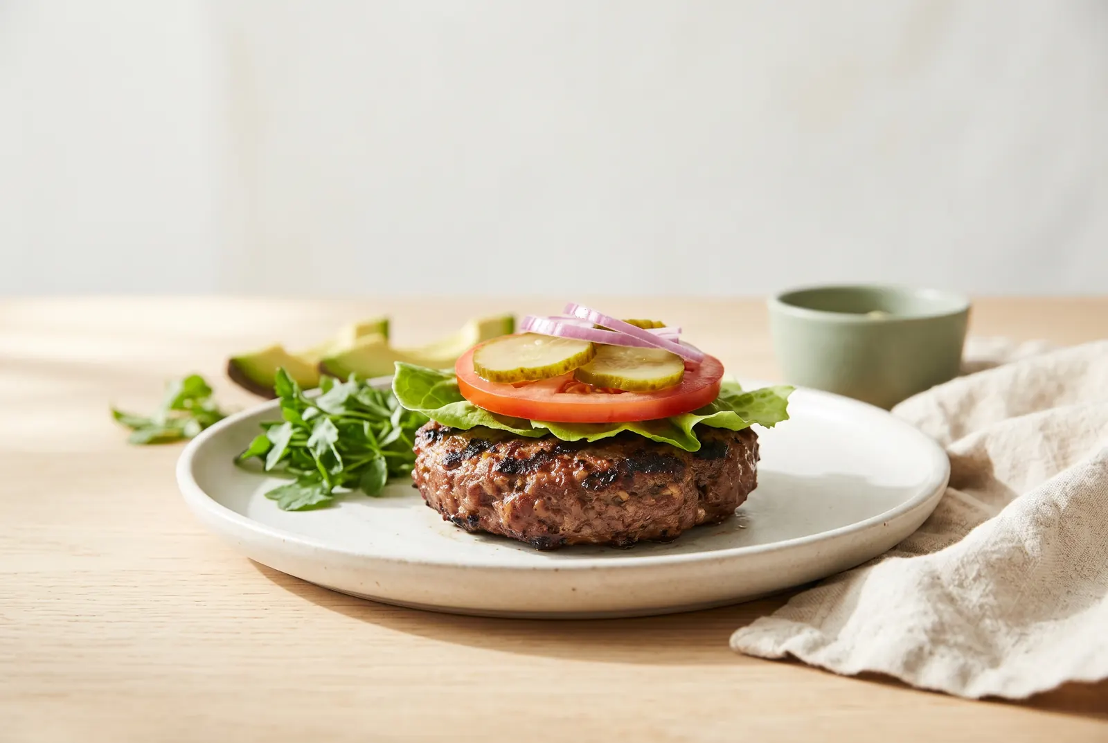 A flame-grilled burger patty with lettuce, tomato, pickles and onion, no bun
