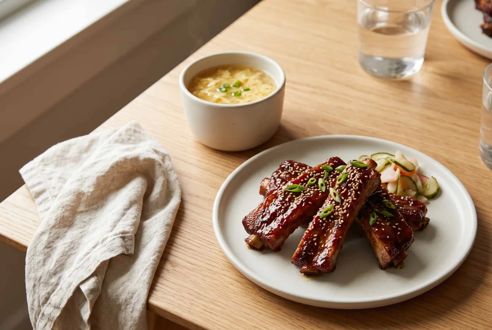 Glazed pork spare ribs beside a small cup of egg drop soup