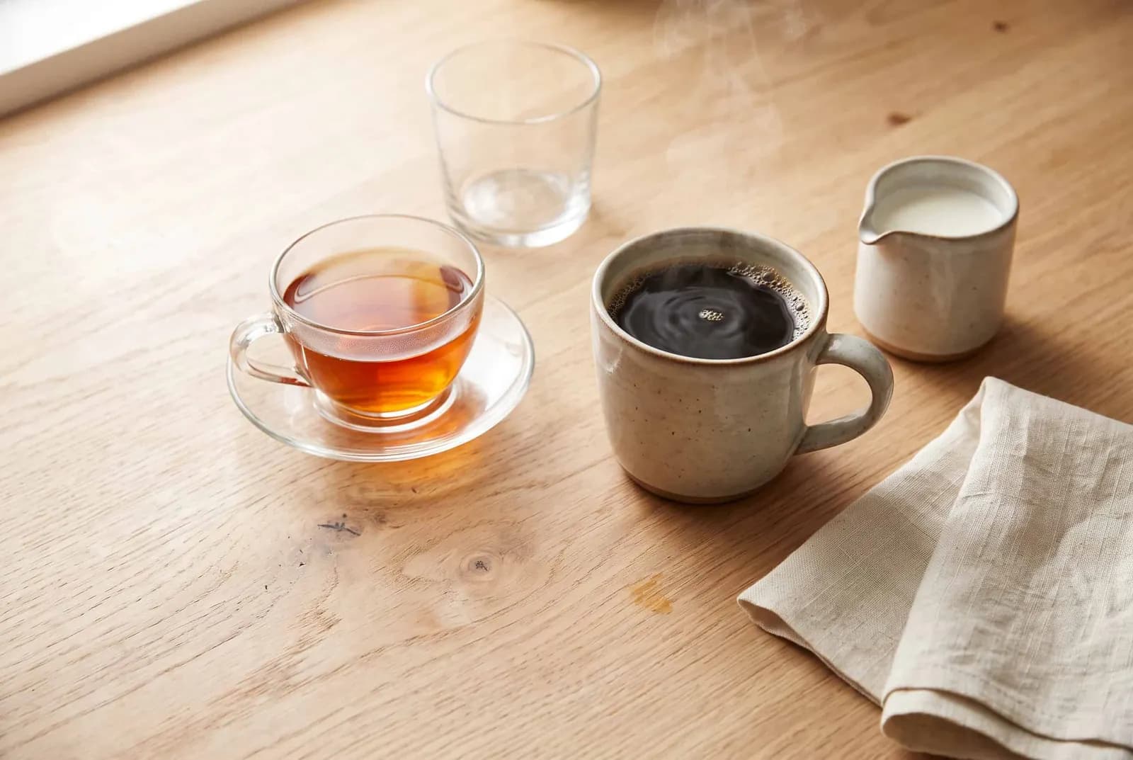 A mug of black coffee, a cup of brewed tea and a small pitcher of cream